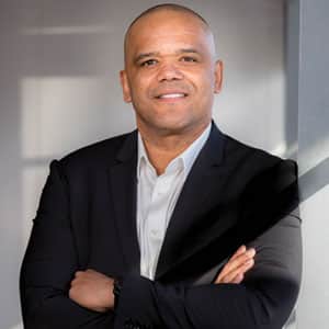 Roy Banks Headshot _ bald Black man with arms crossed in suit with open-neck button up
