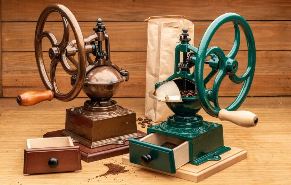 2 Garrett Wade coffee presses with wheel grinder and drawer below with ground coffee. One is brown, one is green. Bag of coffee beans behind grinders. Wood wall behind them.