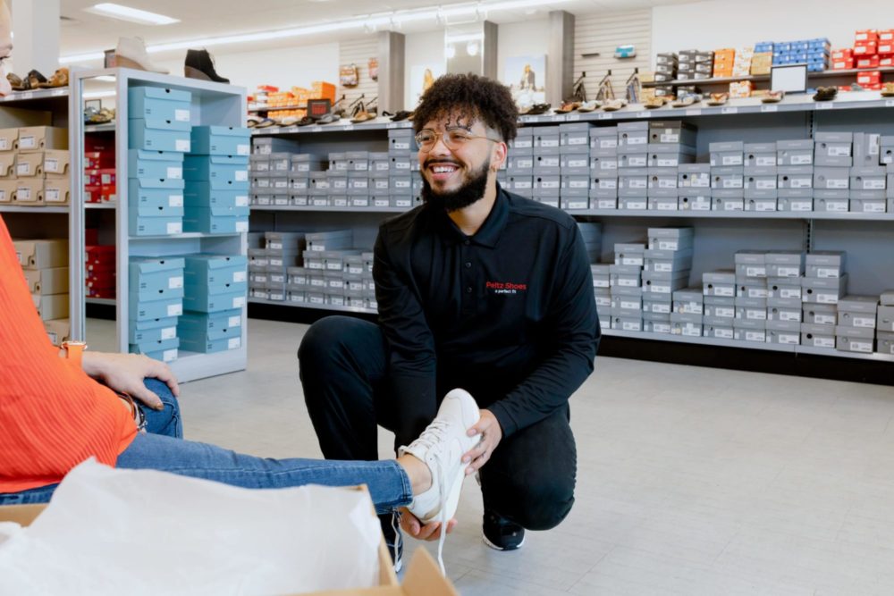 Males sales associate holding foot of woman, helping her try on shoes at Peltz Shoes