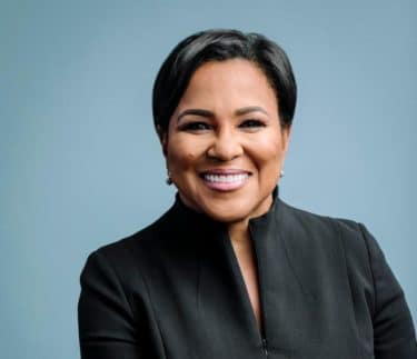 Roz Brewer Headshot _ African American Woman CEO _ Smiling Black woman with short hair in a black suit against a navy blue backdrop
